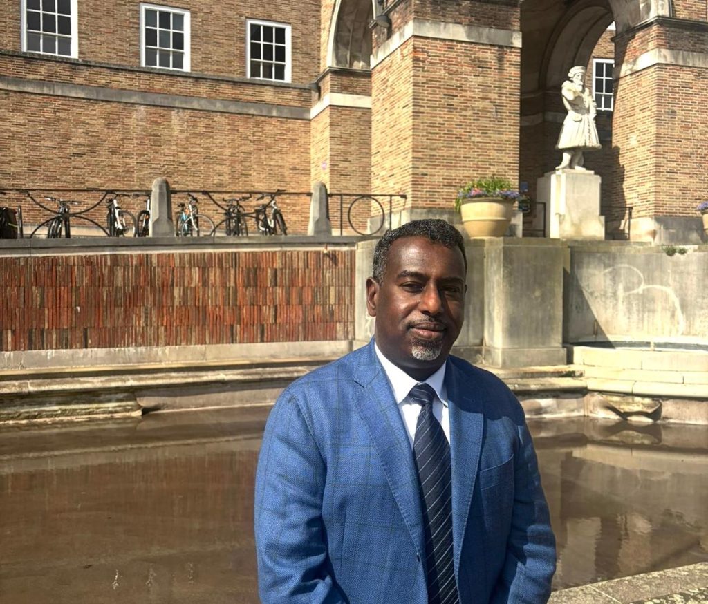Councillor Yassin Mohamud standing in a blue suit outside of Bristol City Hall, in the sun